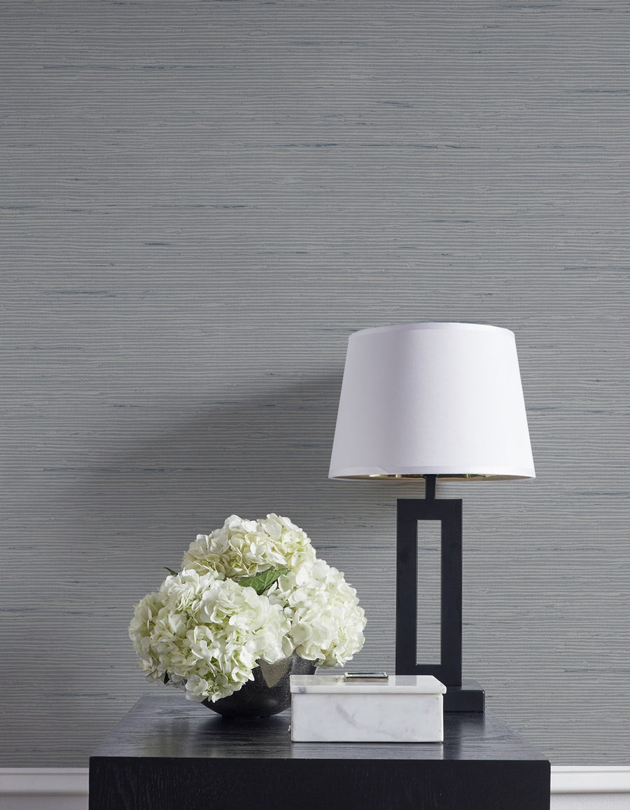 White lamp and floral arrangement on a dark surface against a gray textured wall