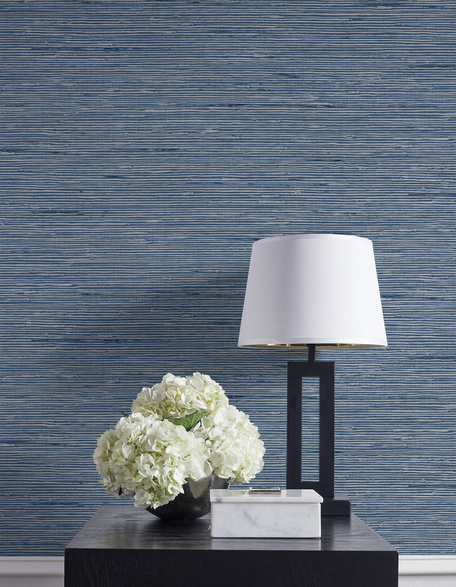 Decorative table with white flowers and lamp against a blue striped wallpaper.