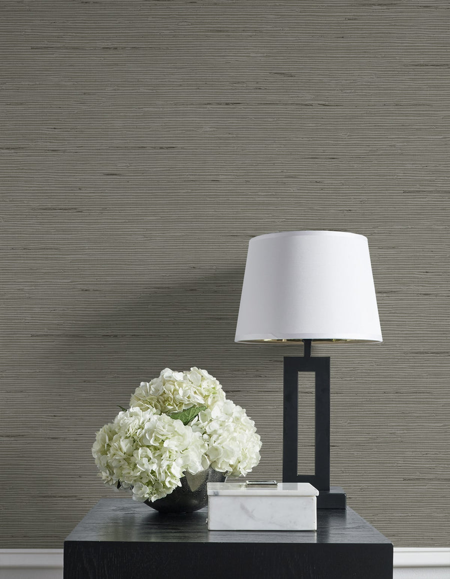 White lamp and floral arrangement on a dark surface against a textured gray wall