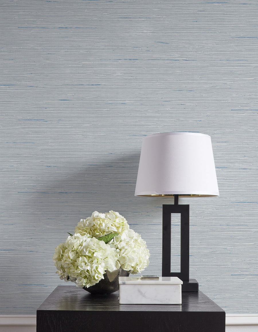 Decorative table with a lamp and floral arrangement against a textured wall.