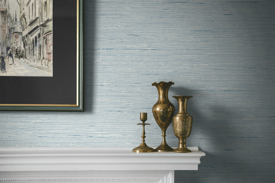 Decorative vases and a candlestick on a mantelpiece with a textured wall and framed artwork in the background.