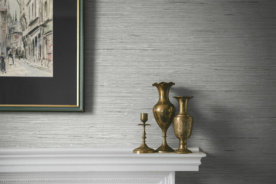 Decorative vases and candlestick on a mantelpiece with a textured wall and framed artwork in the background.