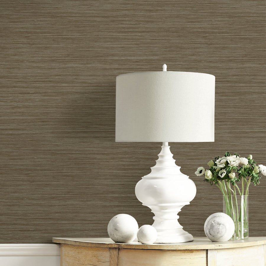 White table lamp on a wooden surface with a vase of flowers against a brown textured wall.