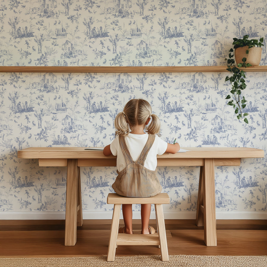 Child sitting at a wooden table against a Blue Village Toile Wallpaper – French Country Life Pattern