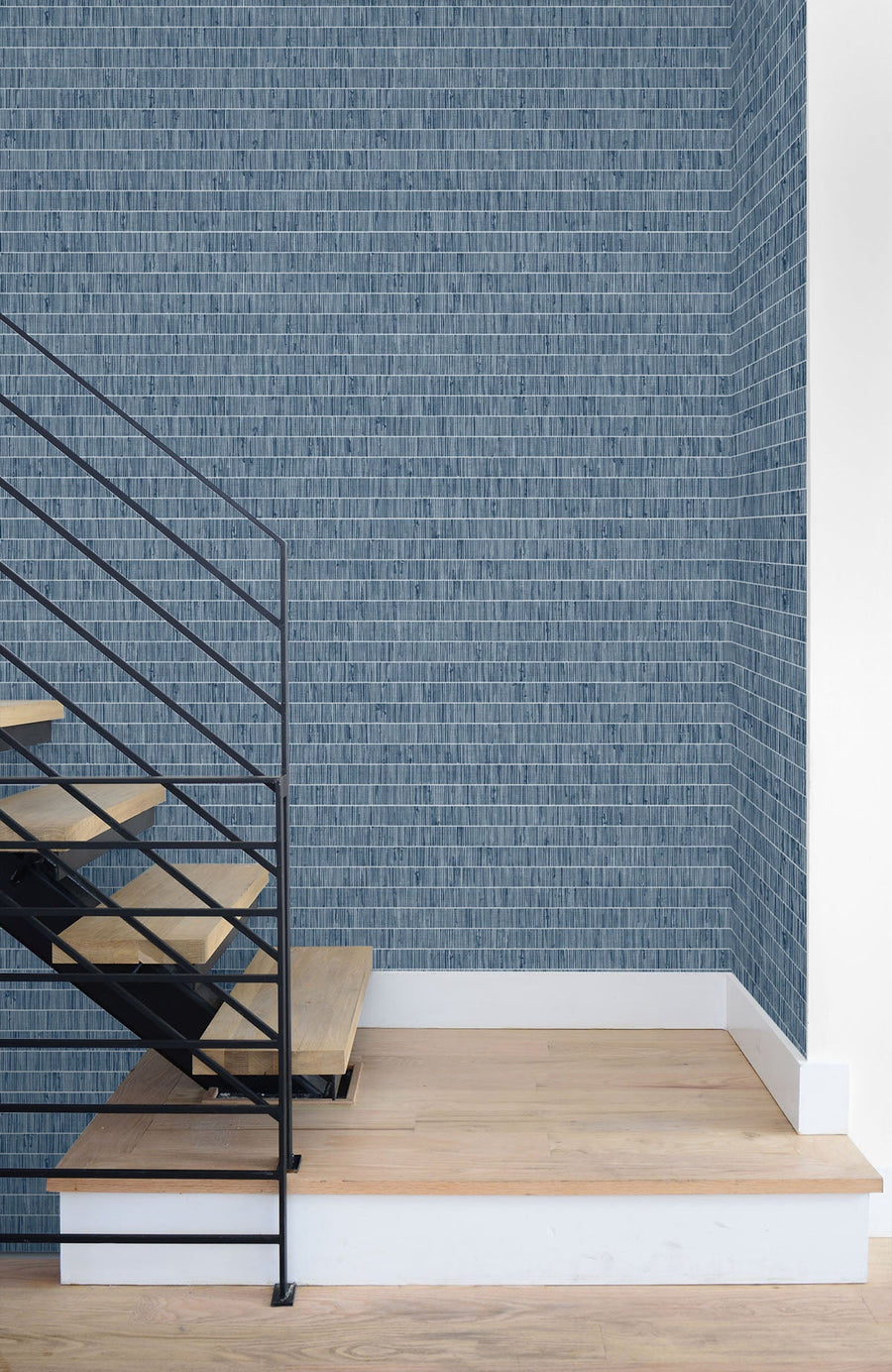 Modern staircase with wooden steps and metal railing against a textured blue wall.