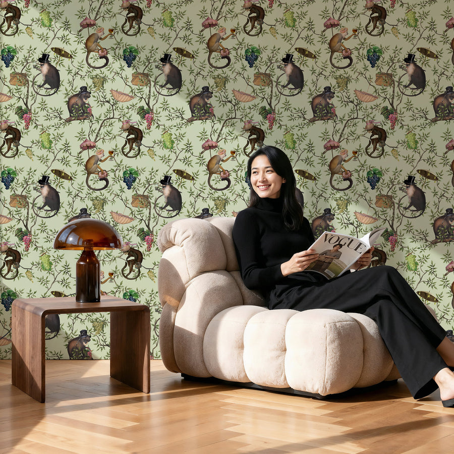 Woman sitting on a beige armchair reading a magazine against a wallpaper with monkey pattern