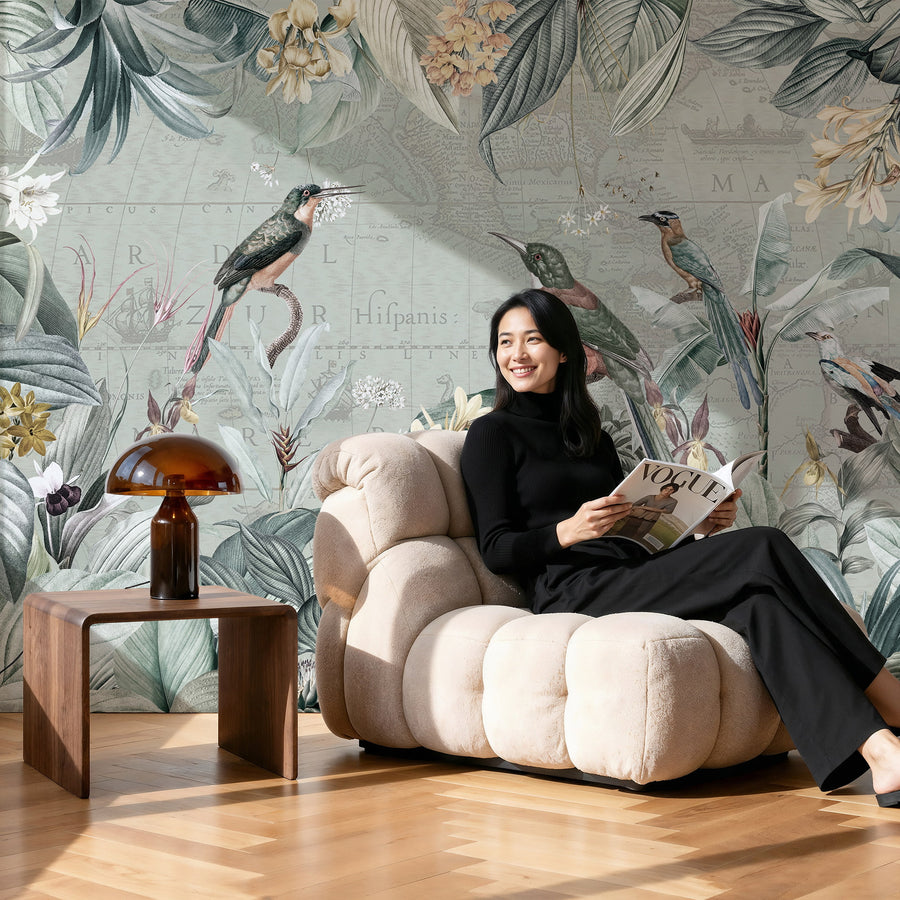 Woman sitting on a beige armchair reading a magazine in a room with Vintage Tropical Map Wall Mural with Birds & Botanicals