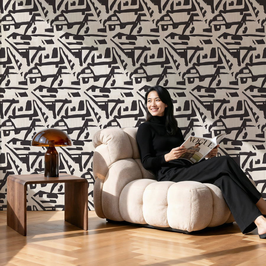 Woman sitting on a modern beige sofa reading a magazine against a Abstract Brushstroke Wallpaper Cream Black