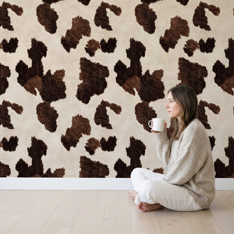 Woman sitting on the floor holding a mug in front of a wall with a Brown Cow Print Wallpaper