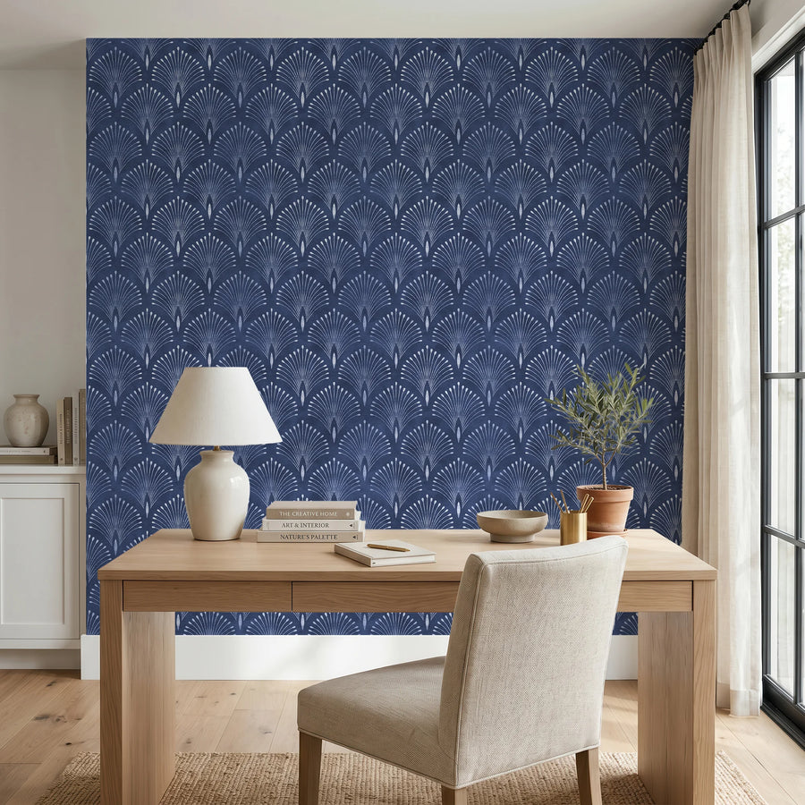 Navy blue Art Deco fan wallpaper in a home office behind a wood desk with a table lamp