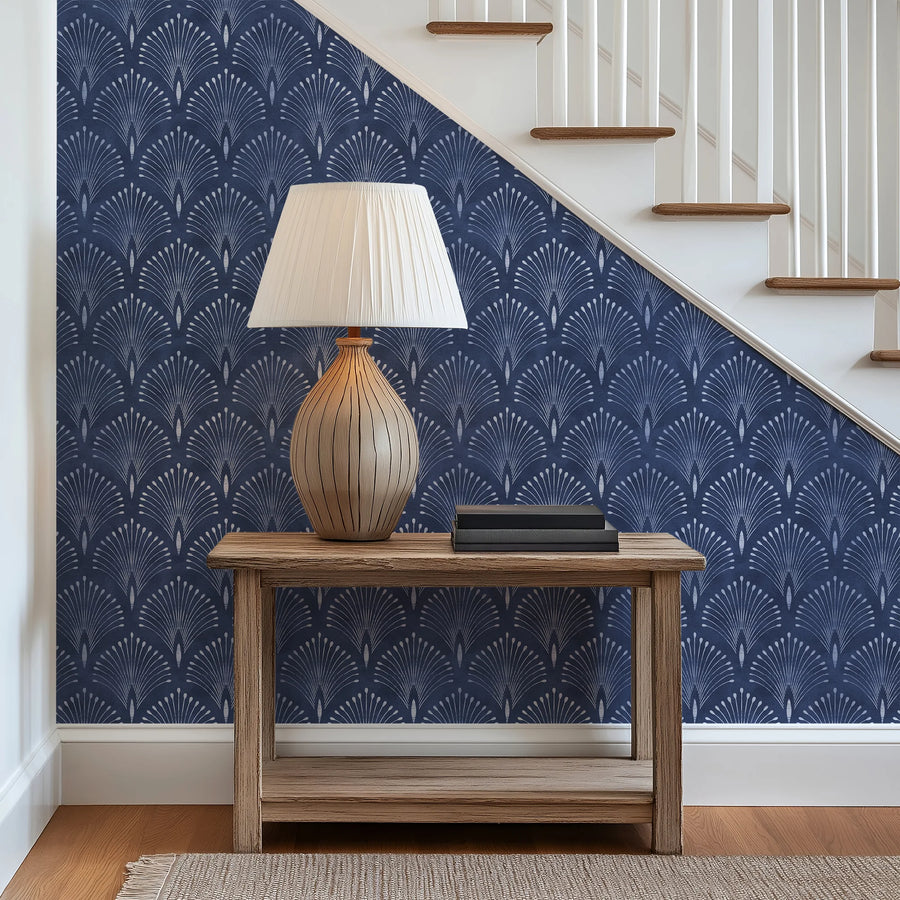 Navy blue Art Deco fan wallpaper on a stairway wall behind a console table and lamp
