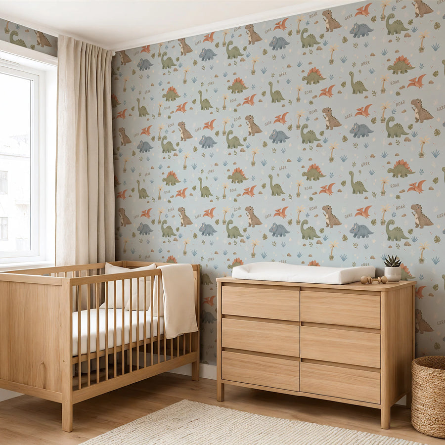 Baby dinosaur nursery wallpaper in powder blue behind a wooden crib and changing dresser by a window