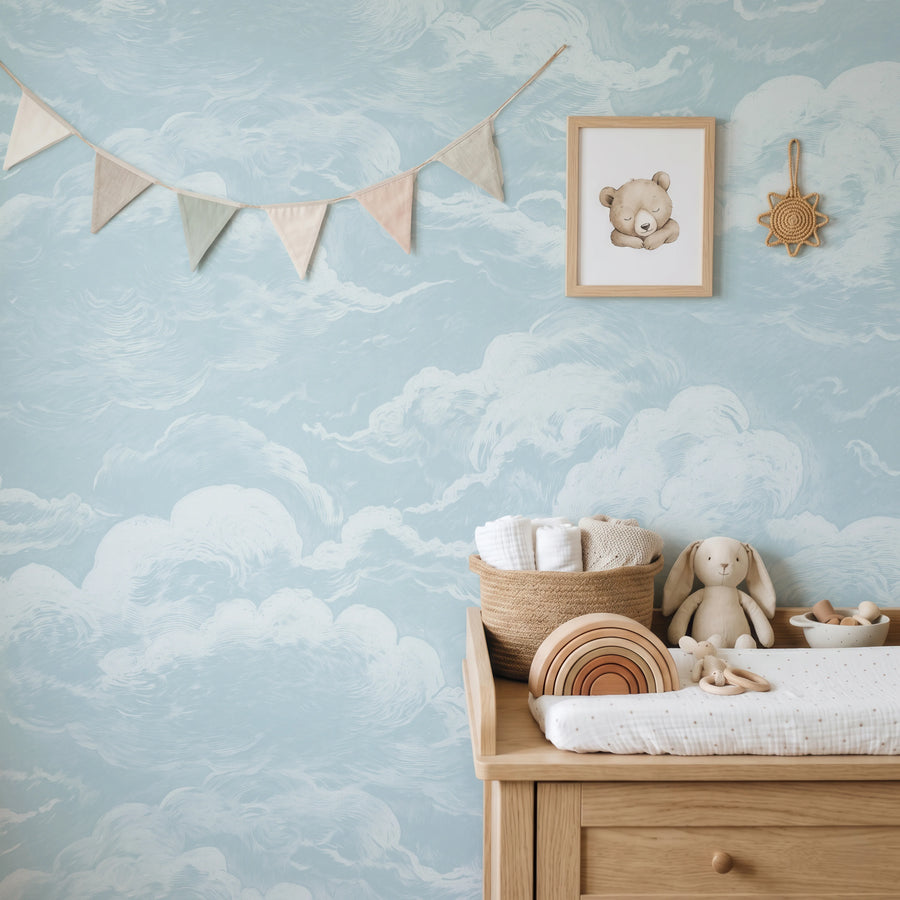 Blue sky and clouds wall mural in a nursery with a changing table and garland