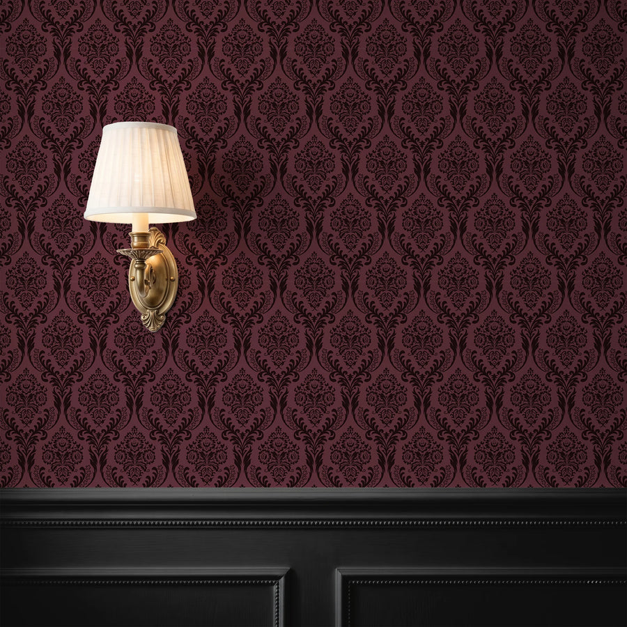 Burgundy damask wallpaper behind a wall sconce with black wainscoting