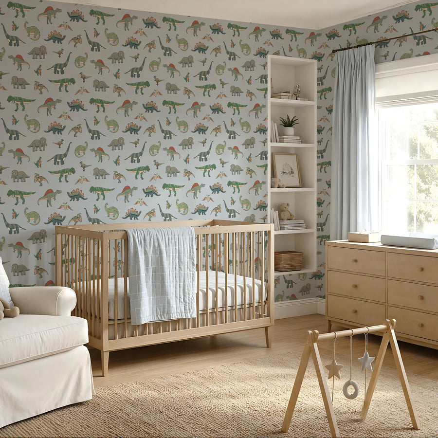 Baby blue dinosaur wallpaper behind a wooden crib, armchair and play gym in a nursery