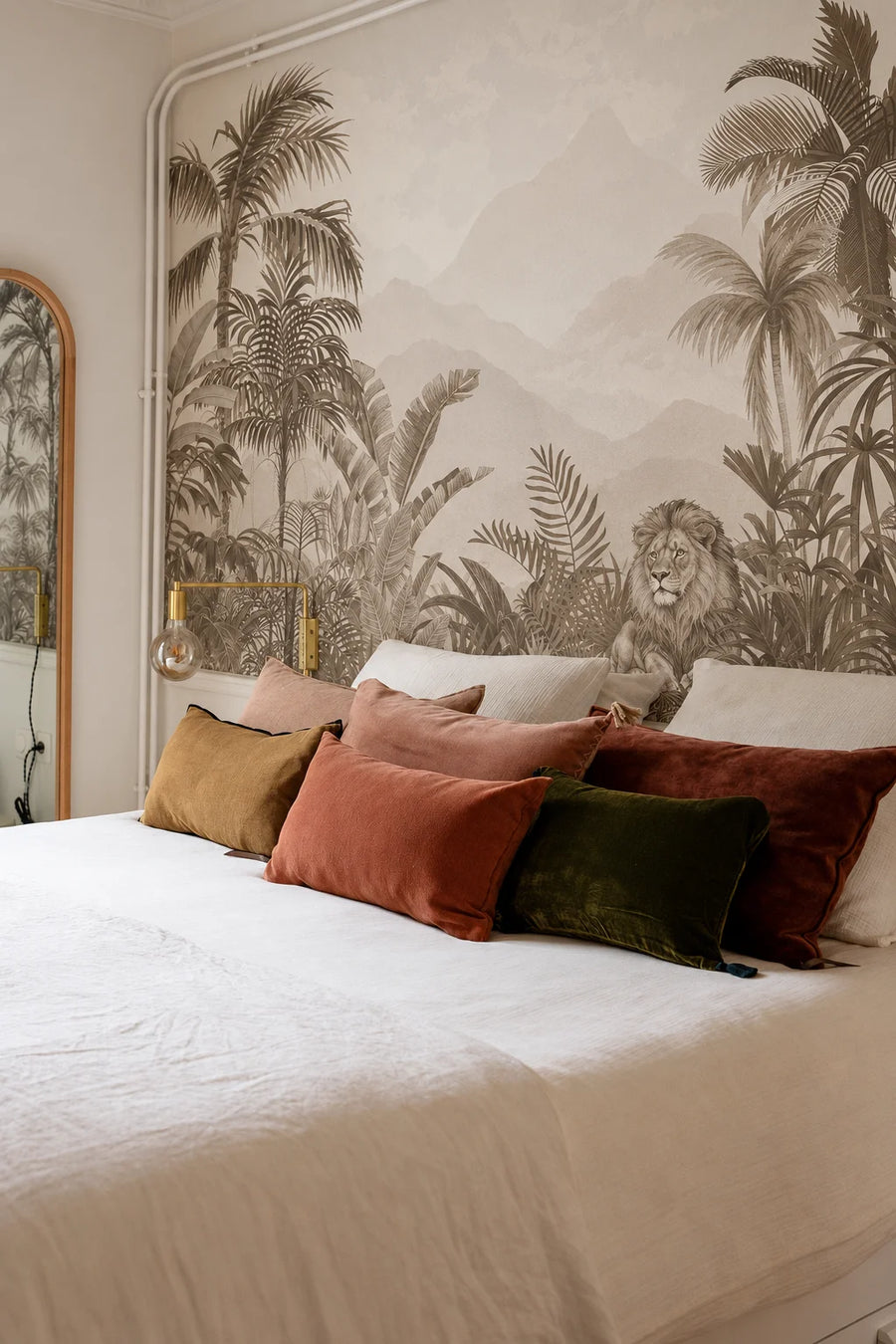 Sepia lion jungle wall mural behind a bed with rust and olive cushions