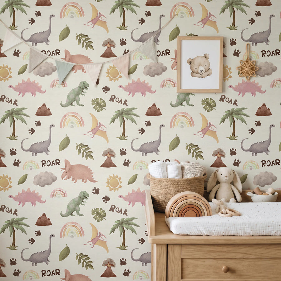Pastel dinosaur and rainbow nursery wallpaper behind a wooden dresser styled with bunting, a bear print and a stuffed bunny