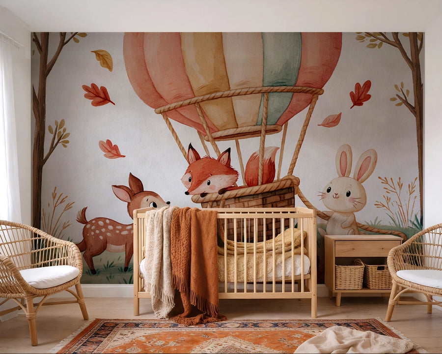 Watercolor woodland animals hot air balloon mural across a nursery wall behind a wooden crib