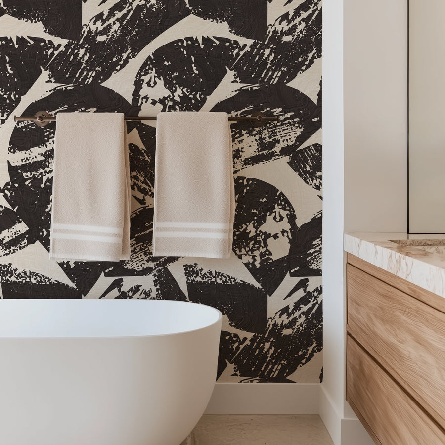 Bathroom with Black and White Abstract Woodcut Wallpaper, round mirror, and brown ottomans., white freestanding bathtub, and wooden cabinets.
