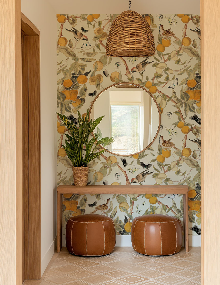 Decorative hallway with Vintage Citrus Wallpaper – Orange Tree, Birds & Butterflies, round mirror, and brown ottomans.