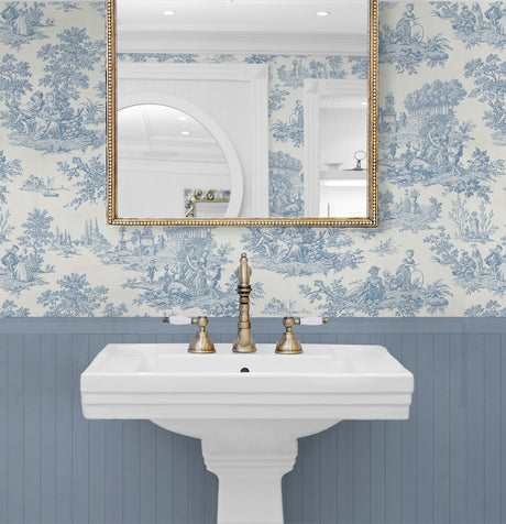 Bathroom with white pedestal sink, gold fixtures, and blue toile wallpaper.