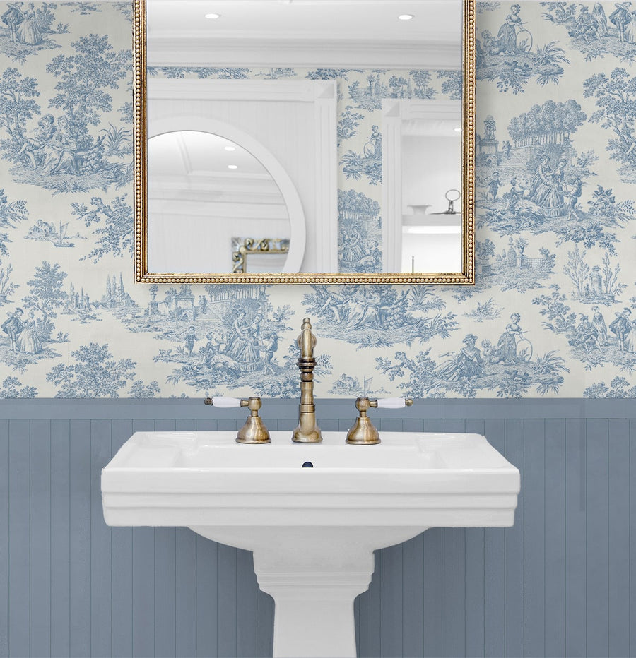 Bathroom with white pedestal sink, gold fixtures, and blue toile wallpaper.