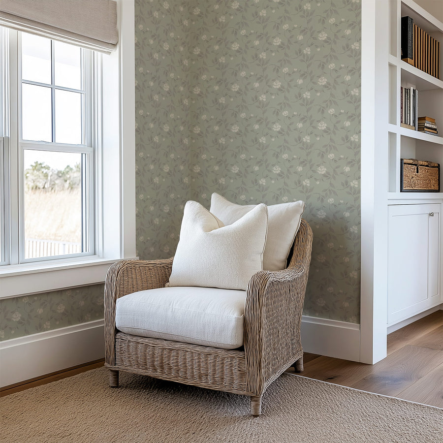 Wicker chair with white cushions in a room with floral wallpaper and a window.