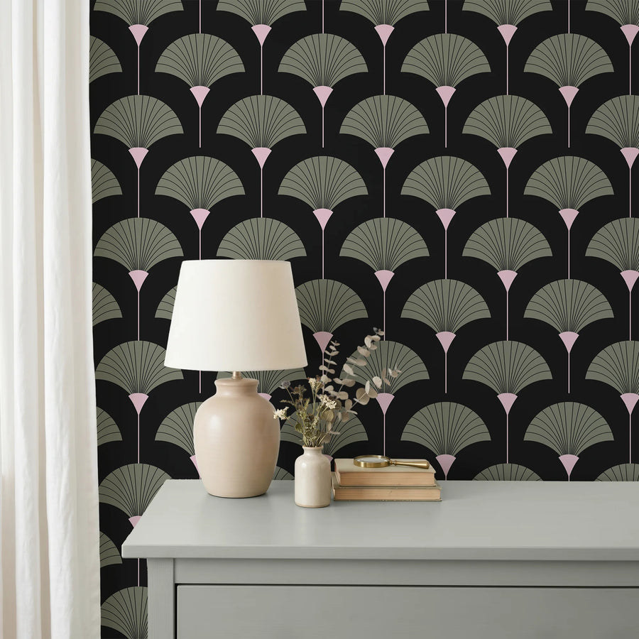 Sage green and black Art Deco fan wallpaper behind a dresser with a cream lamp and eucalyptus