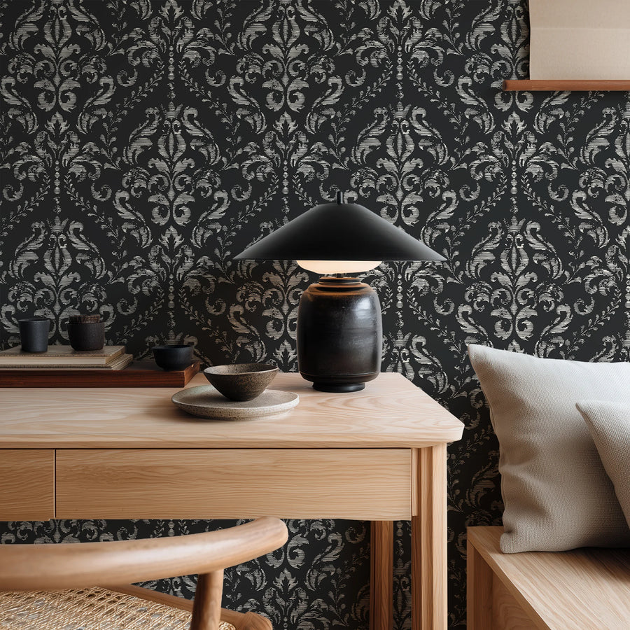 Black distressed damask wallpaper behind a wood console with a black dome lamp