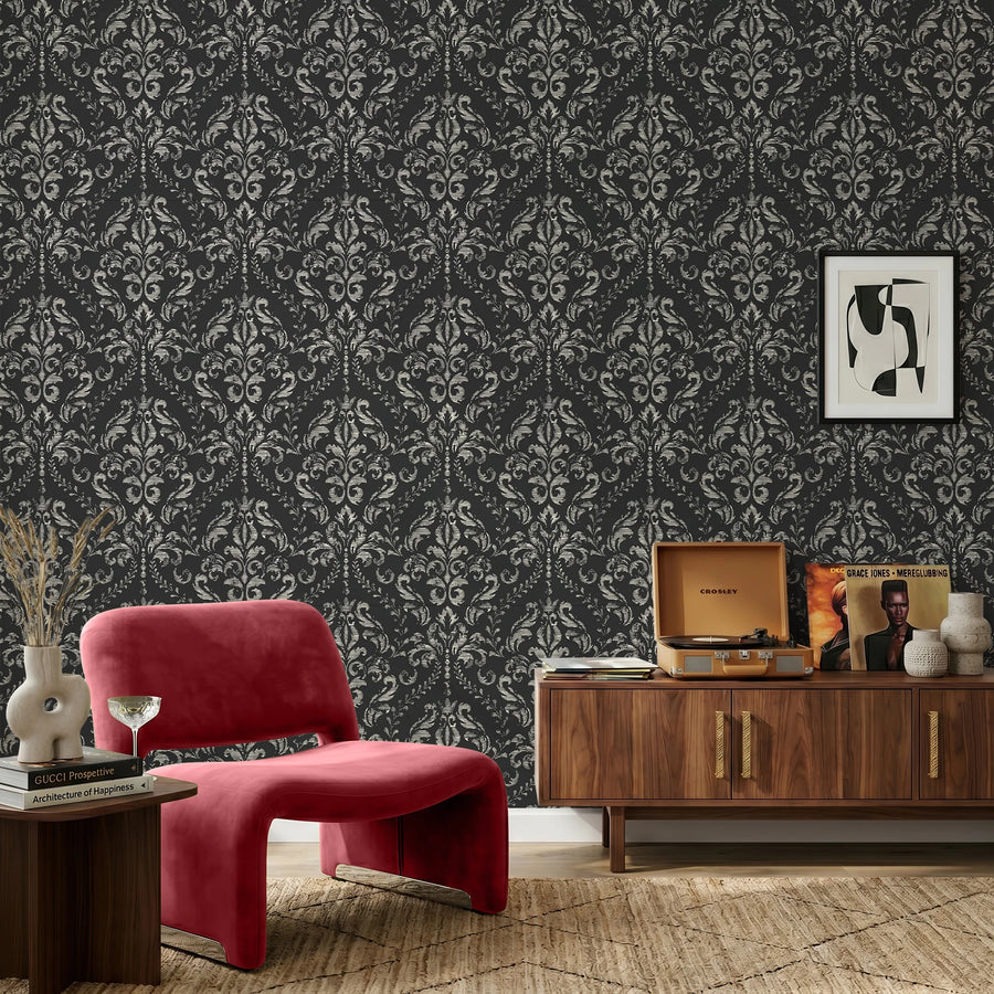 Black distressed damask wallpaper behind a red accent chair
