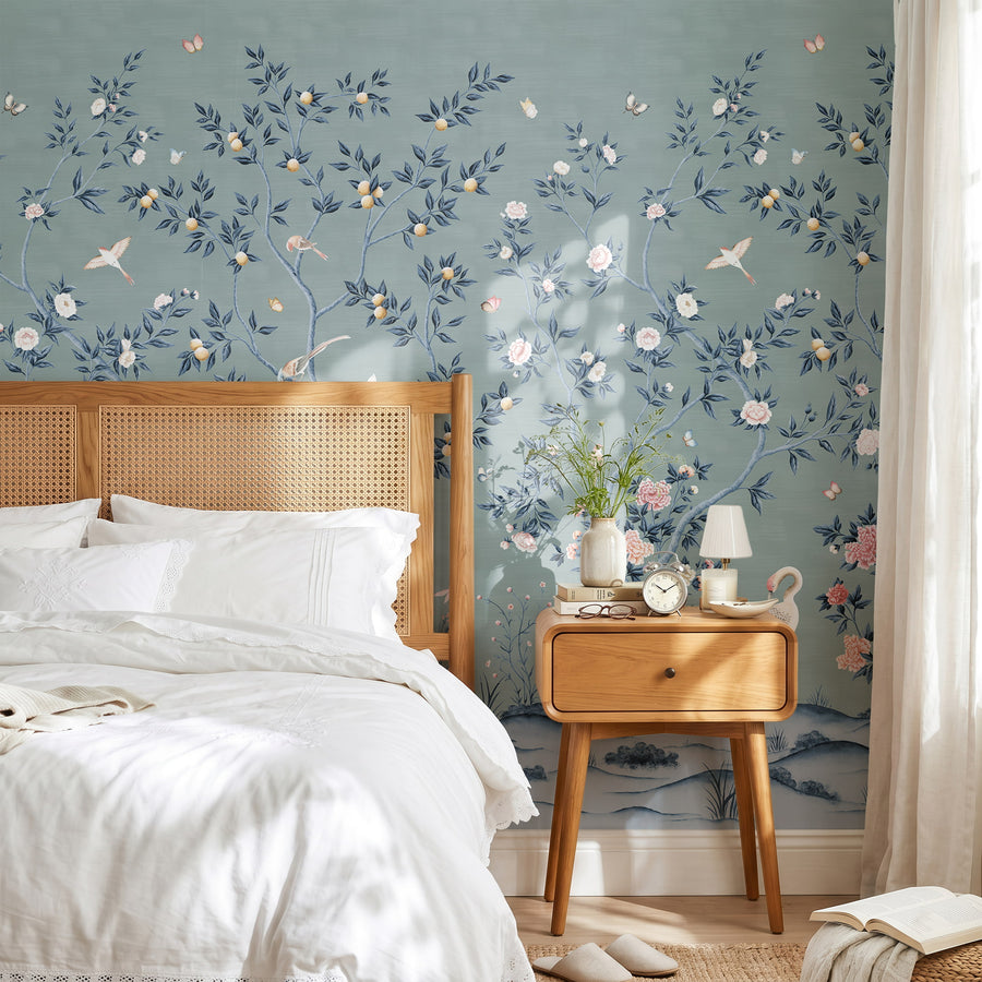 Blue chinoiserie wallpaper mural with cranes and blossoms in a bedroom behind a rattan bed