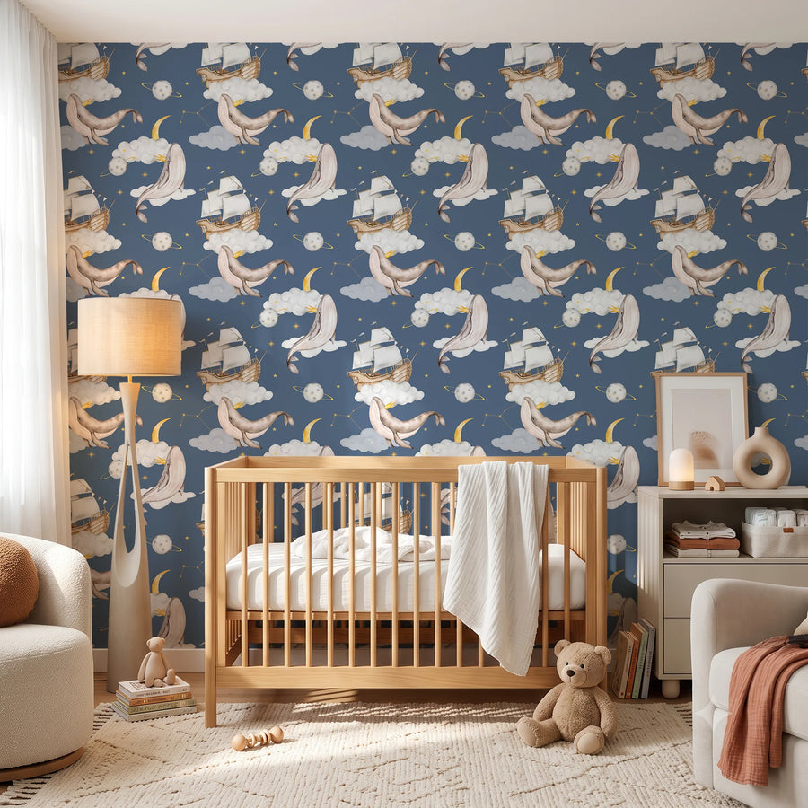 Navy whale and moon nursery wallpaper behind a wooden crib with a teddy bear