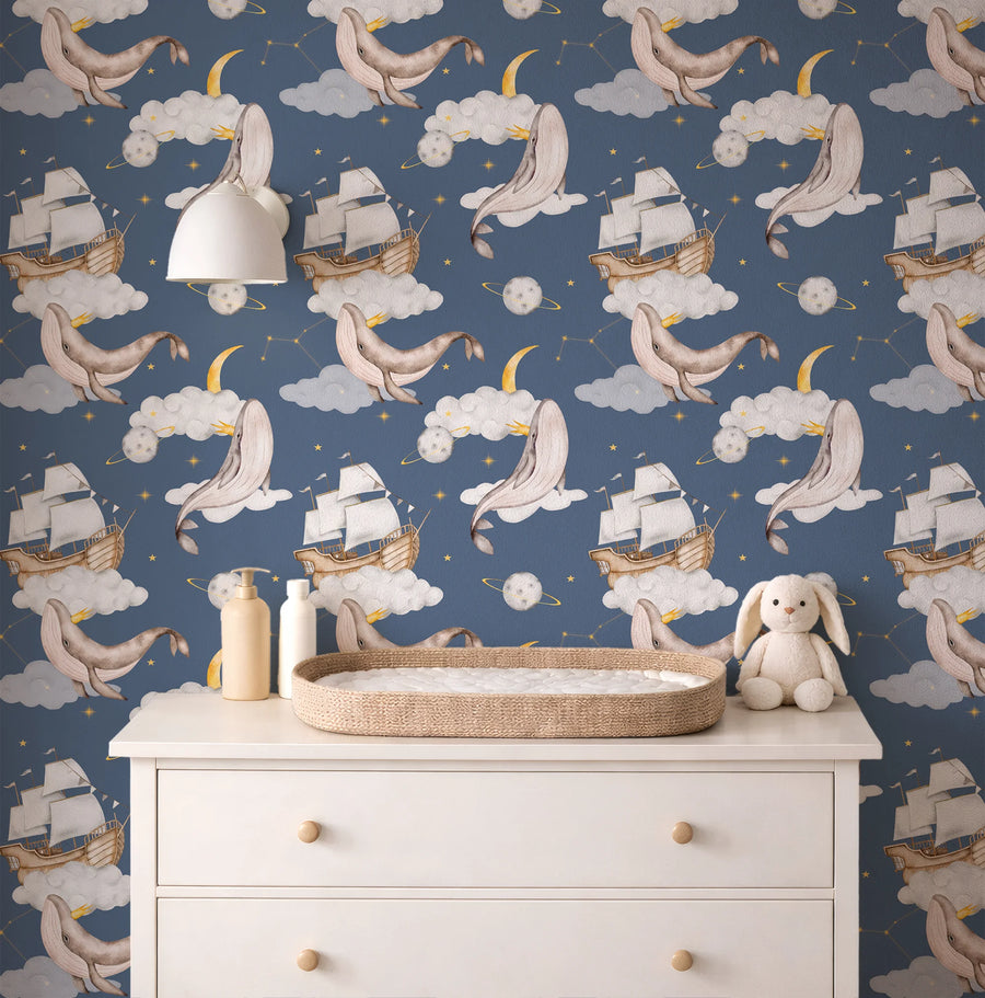 Navy celestial whale nursery wallpaper behind a white dresser with a changing basket and plush bunny