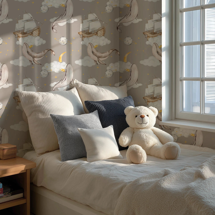 Celestial whale wallpaper with clouds and stars behind a bed with cushions and a teddy bear