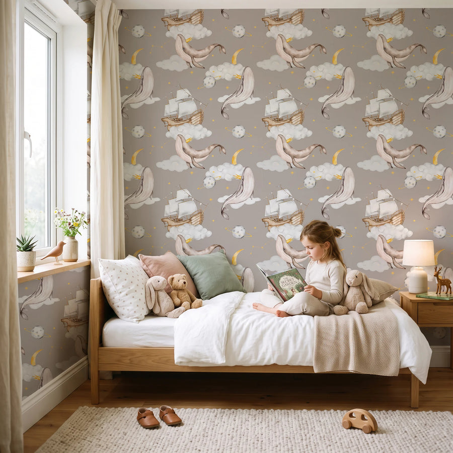 Celestial whale nursery wallpaper on taupe in a child's bedroom with a girl reading on the bed