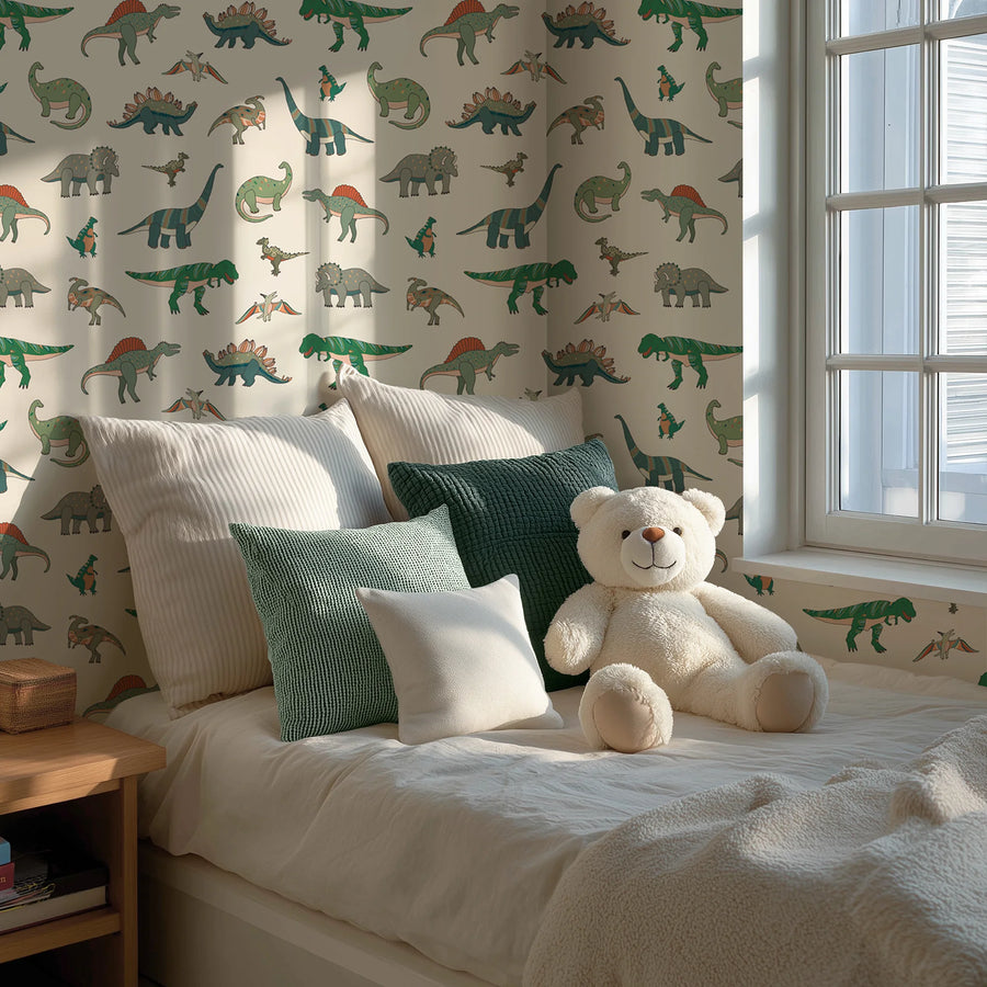 Cartoon dinosaur kids wallpaper in green and cream behind a bed with green pillows and a teddy bear by the window