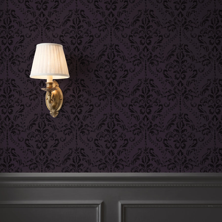 Gothic purple damask wallpaper behind a brass wall sconce with dark wainscoting