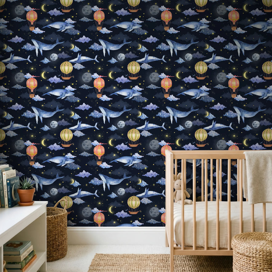 Hot air balloon and whale nursery wallpaper on navy behind a wooden crib