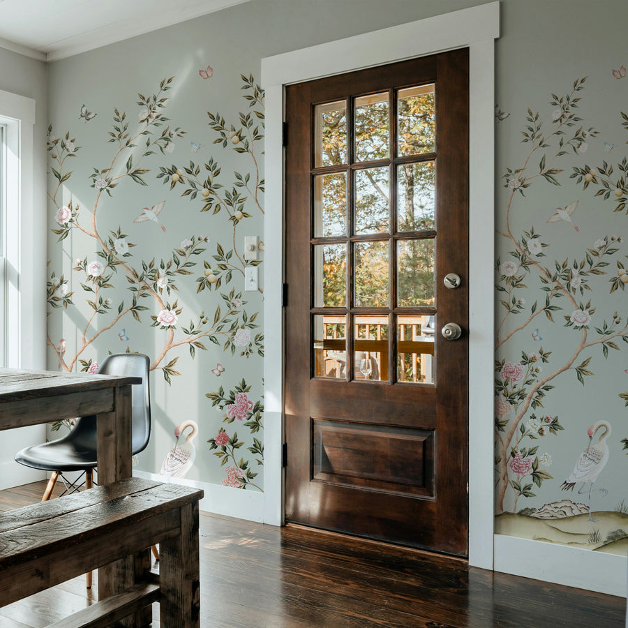 Light blue chinoiserie crane wallpaper mural in an entryway beside a wood door