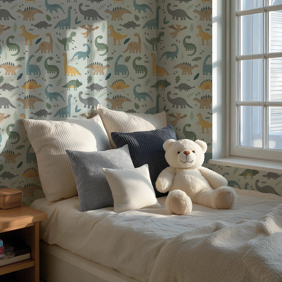 Light blue dinosaur wallpaper for kids behind a bed with pillows and a teddy bear by the window