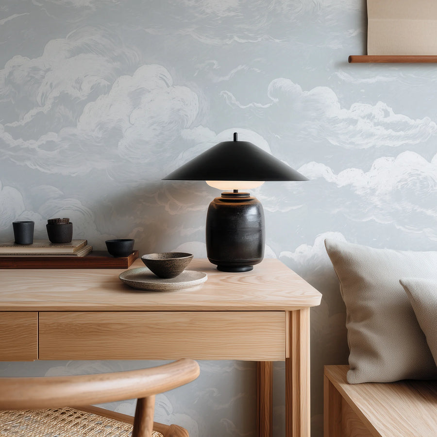 Light blue sky and clouds wall mural behind a wood desk with a black lamp
