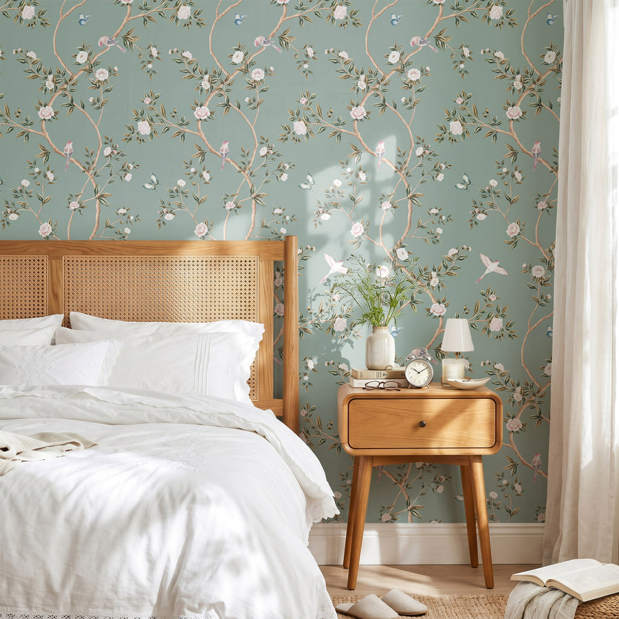 Bedroom with cane headboard wood nightstand and white bedding featuring Light Green Chinoiserie Hemma Wallpaper Floral Garden Birds by Maja Pitschmann