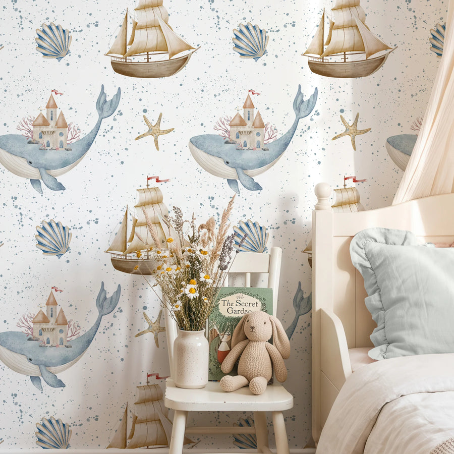 Nautical nursery wallpaper with watercolor whales and sailboats behind a child's chair with a storybook and plush bunny