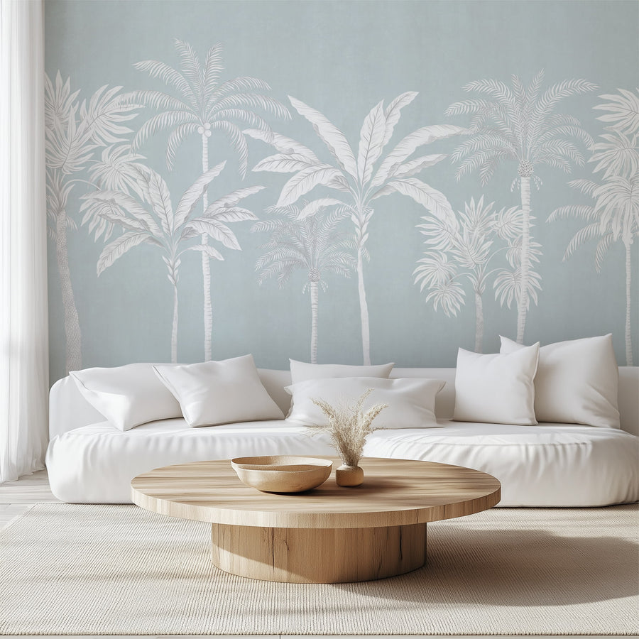 Pastel blue palm tree tropical wallpaper mural in a living room behind a white sofa