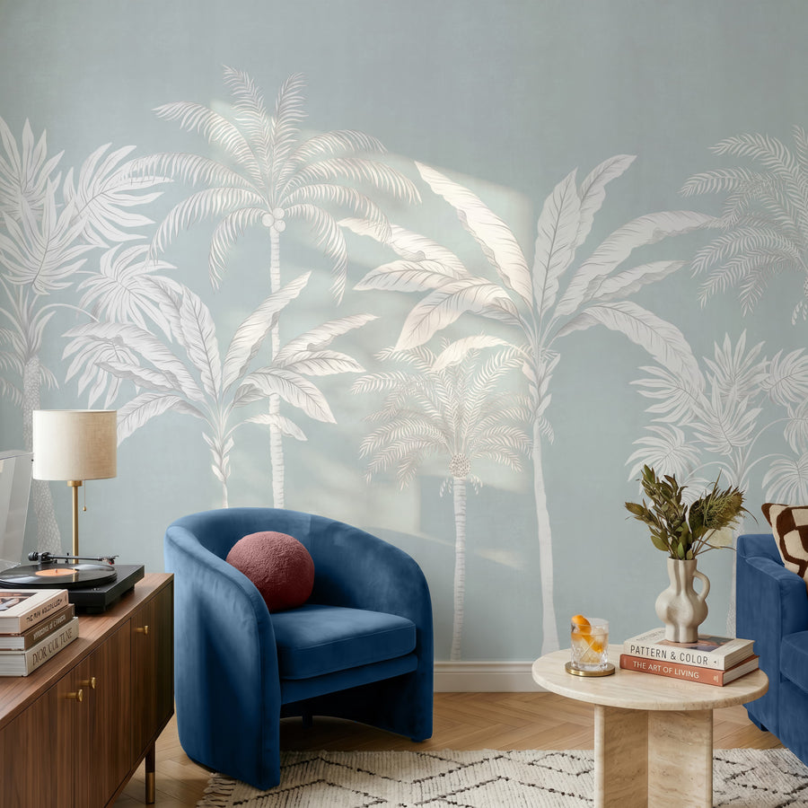 Pastel blue palm tree mural in a sitting room behind a navy blue armchair