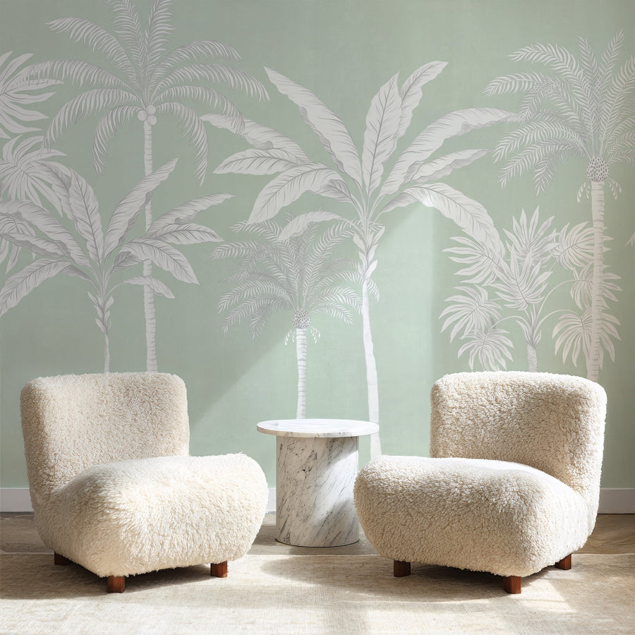 Sage green palm tree mural in a sitting room behind two boucle armchairs
