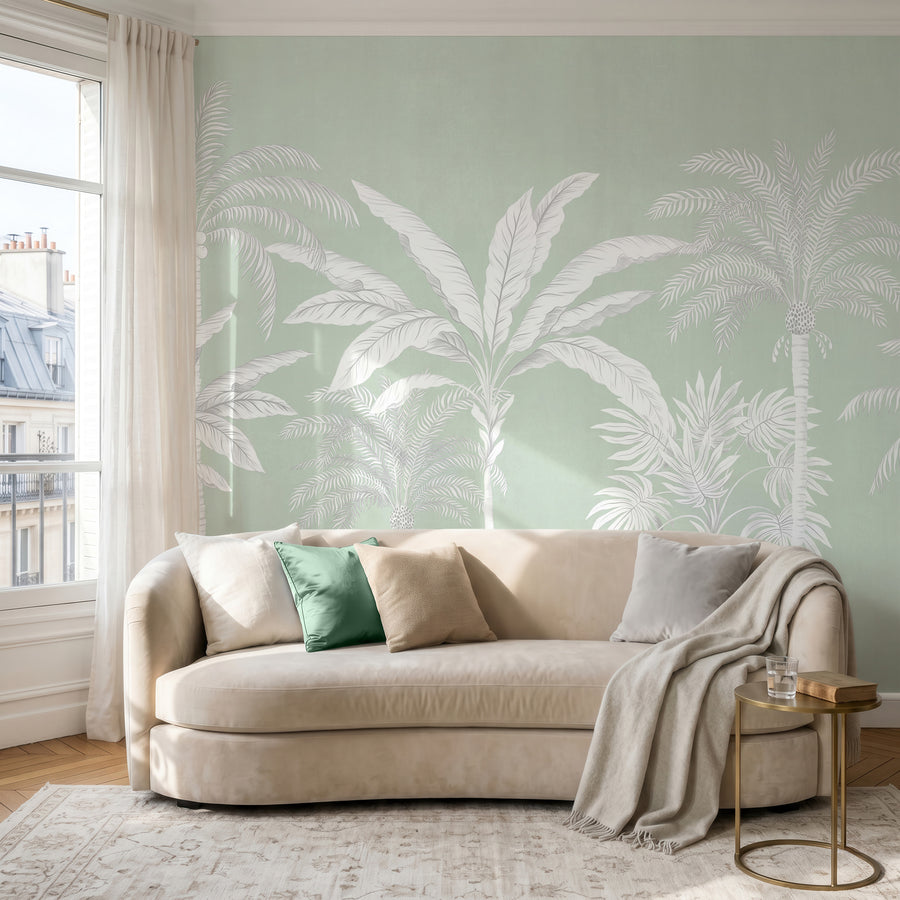 Sage green palm tree wallpaper mural with white palms in a living room behind a velvet sofa