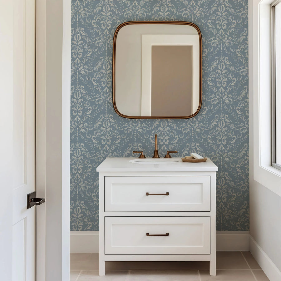 Vintage blue damask wallpaper in a bathroom with a white vanity and mirror