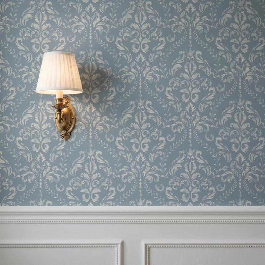 Vintage blue damask wallpaper behind a wall sconce with white wainscoting