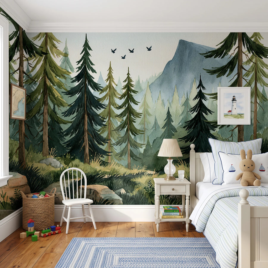Watercolor mountain forest wall mural by Uta Naumann in a kids bedroom with a white chair, bed and blue rug